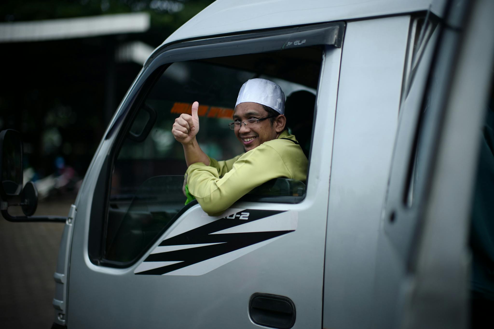 Cheerful driver inside a van in Surabaya, Indonesia, showing a thumbs-up gesture.